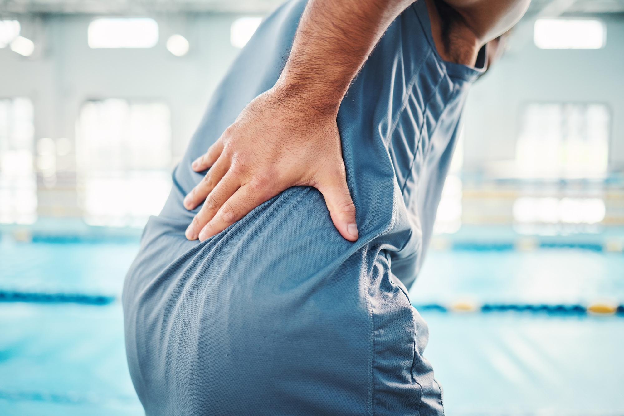 Pain in back, sports and man by swimming pool with injury, muscle ache and inflammation from traini